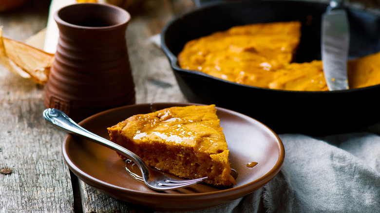 A slice of cornbread is on a plate with a skillet in the background.
