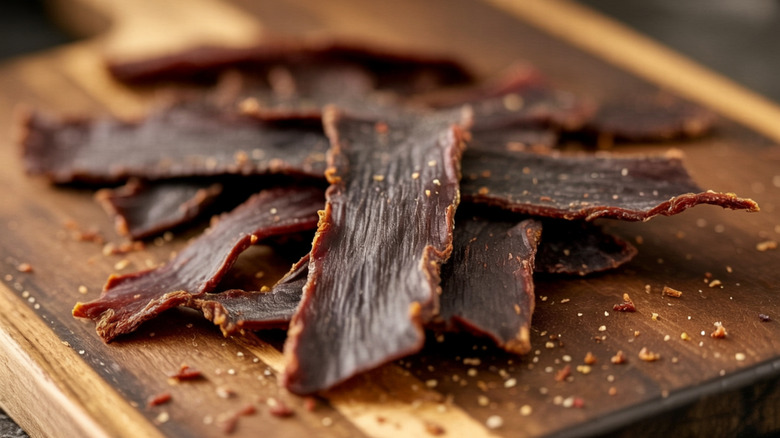 Strips of beef jerky are piled on a wooden cutting board.