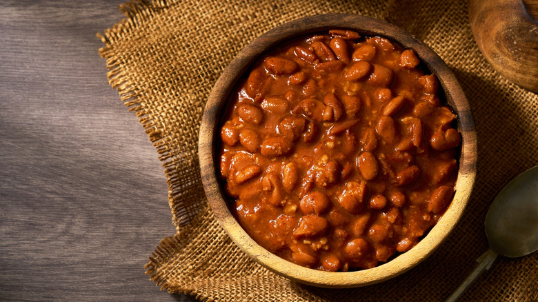 A wooden bowl is filled with baked beans.