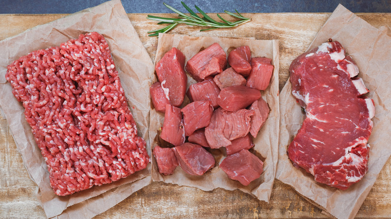A wood cutting board has different types of raw meat on top.