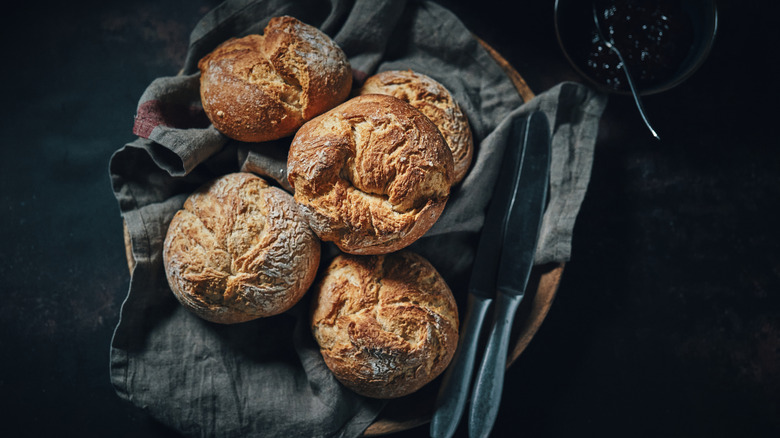 A plate of sourdough rolls on a grey napkin is on a table.