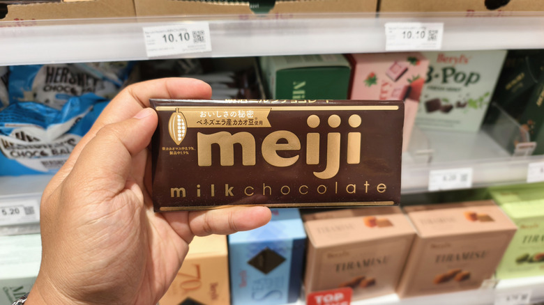 A hand holding a bar of Meiji milk chocolate