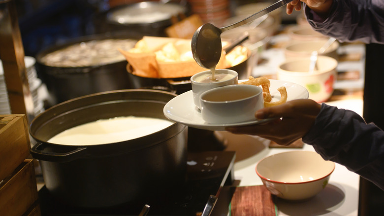 A hand ladling soup into a bowl at a table with pots of soup