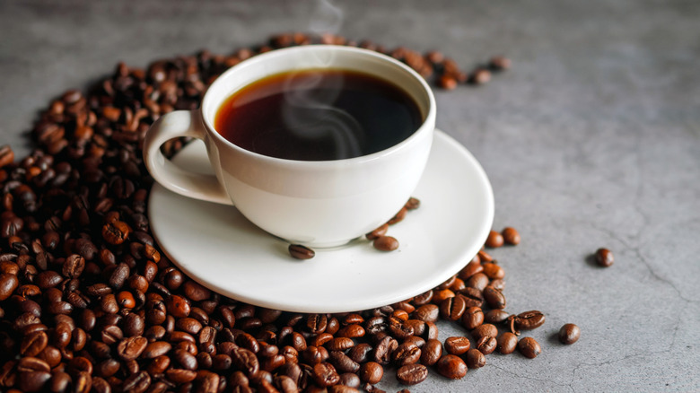 Cup of steaming coffee on coffee beans