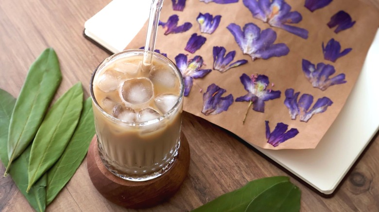 Iced coffee with straw next to purple flower painting