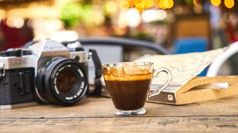Glass cup of espresso on table with camera and book