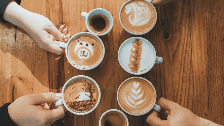 Wooden table with people reaching for various coffee drinks