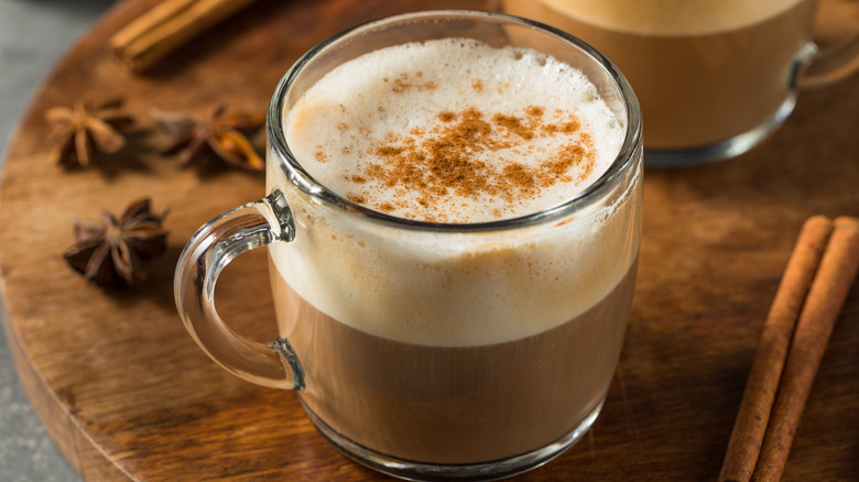 Dirty chai in glass mug with spices on wooden board