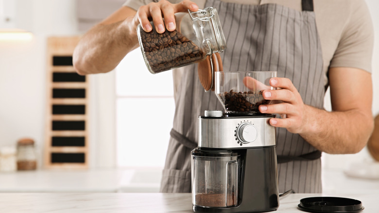 Person pouring coffee beans into a coffee grinder