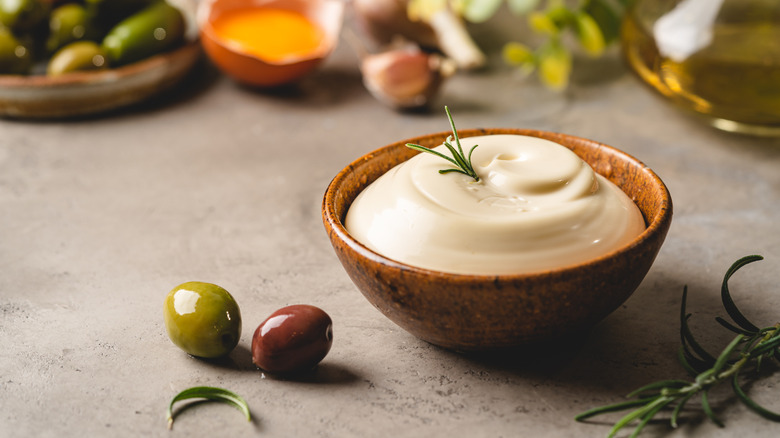 Small bowl of mayonnaise on surface with olives