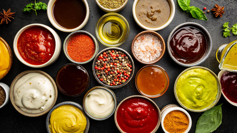 Various jars & containers of sauces & oils on black background