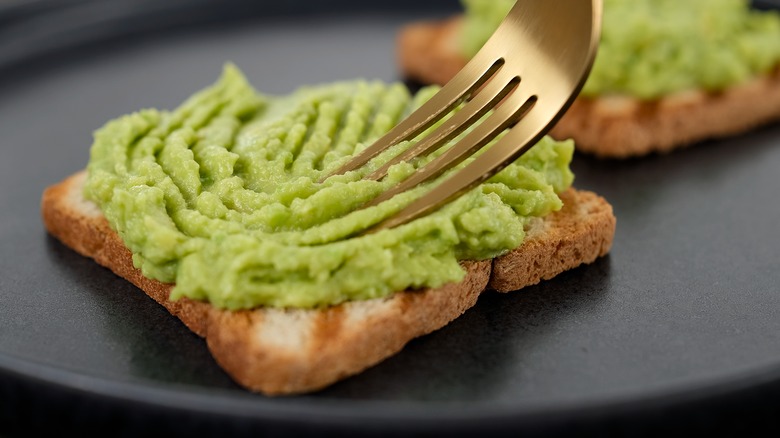fork spreading avocado on bread