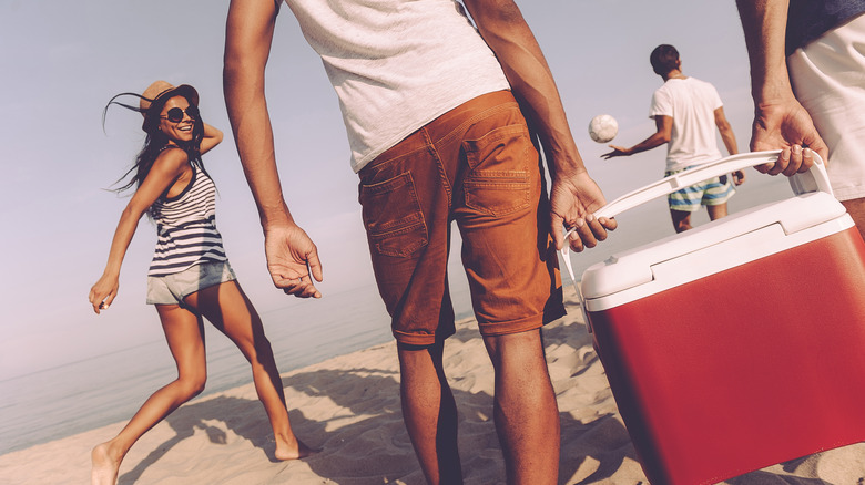 people carrying a cooler on the beach