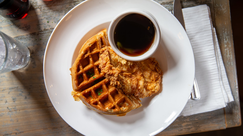 Top down view of chicken and waffles on a white plate with a bowl of maple syrup.