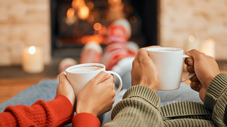 Couple drinking coffee in front of a fireplace 