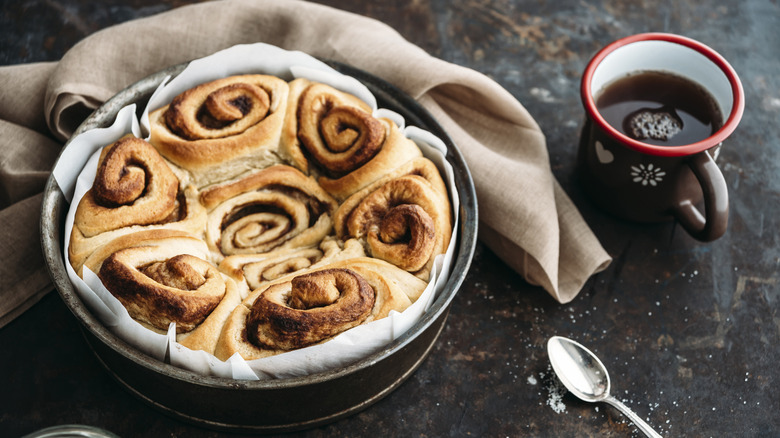 Cinnamon rolls in round baking pan with cup of coffee