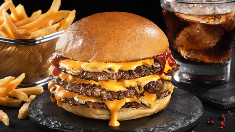A plate with a cheeseburger next to fries and cola