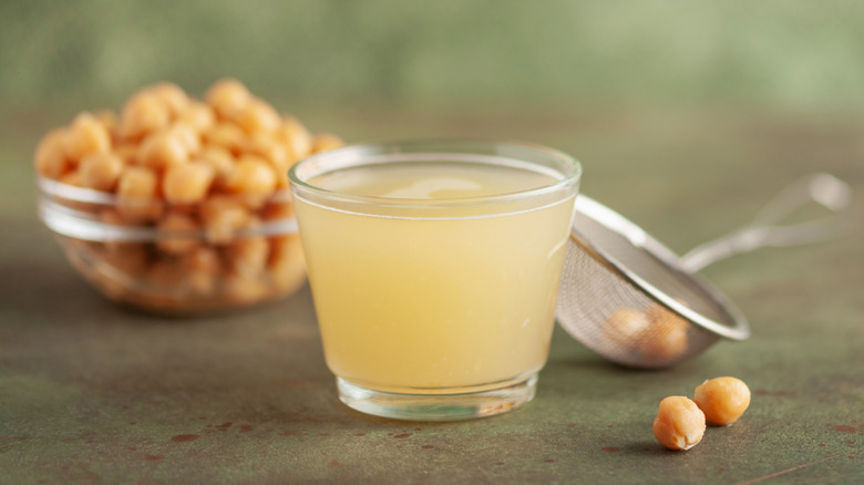 Cup of aquafaba in front of bowl of chickpeas