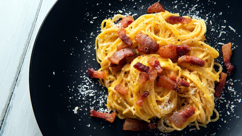 Pasta carbonara on a black plate with white wooden table background