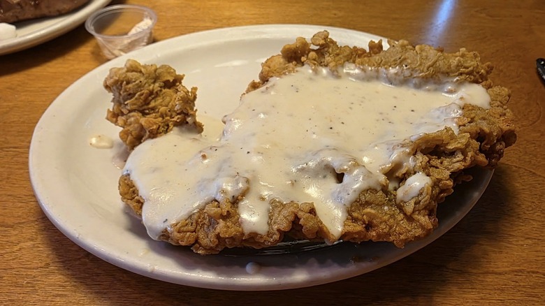 A Texas Roadhouse country fried steak, covered in white gravy on a white plate on a table