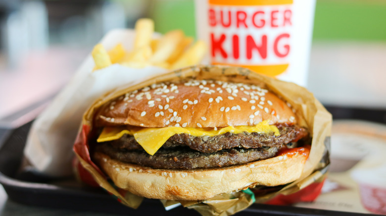 A Burger King burger with two patties and cheese in front of Burger King cup and fries