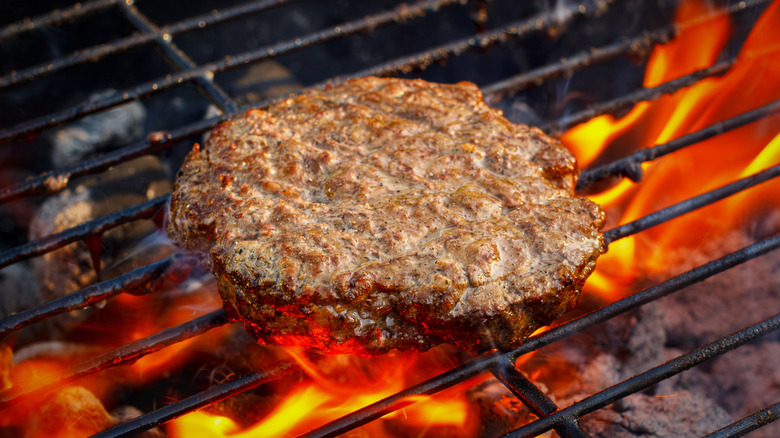 A burger patty on a grill, under flames
