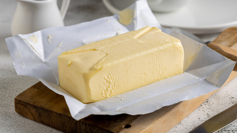 Stick of open butter on a cutting board with wrapper