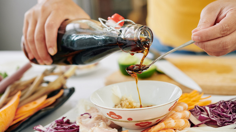 A person pours soy sauce into a bowl