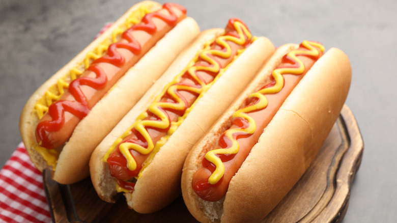 Three hot dogs with ketchup and mustard zigzagged on the top, on a serving tray