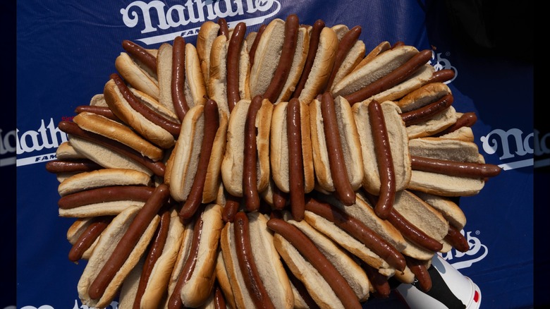 A pile of plain hot dogs in buns on a Nathan's Famous backdrop