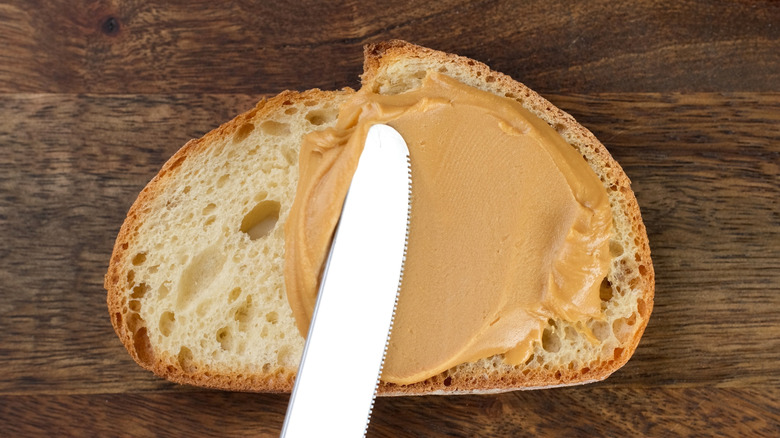 Peanut butter being spread onto slice of bread with knife