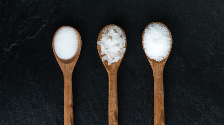 Three wooden spoons each with a different type of salt in them on a black background