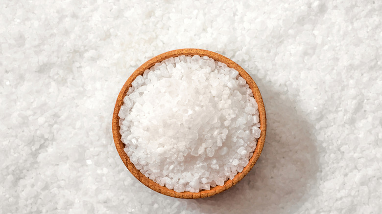 A small wooden bowl of sea salt on a bed of white sea salt.