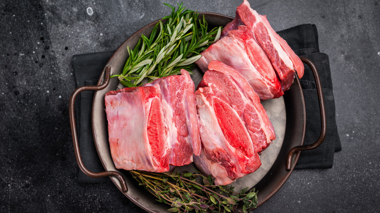 Cuts of raw beef short rib in a pan with springs of seasoning