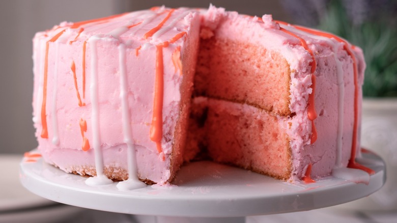 A pink cake on a stand with one slice removed