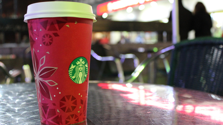 A red Starbucks holiday cup with a snowflake design sits on a table in a cafe.