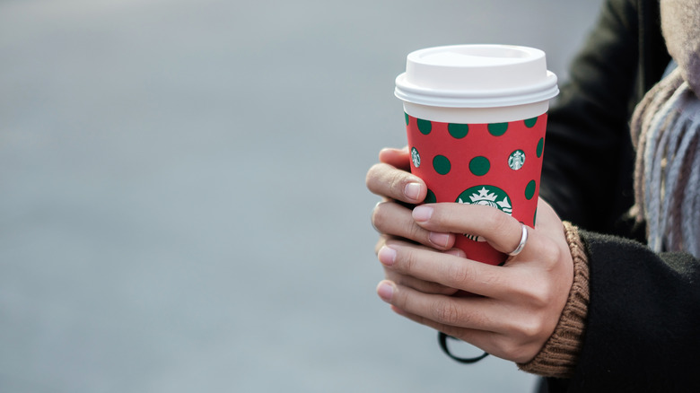 A woman holds a holiday Starbucks cup that is red with green polka dots.