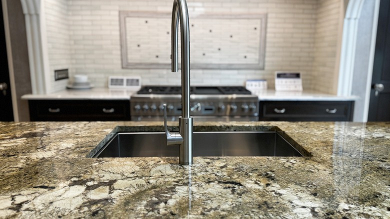 Close-up of an island sink in a granite countertop with a blurred range in the background