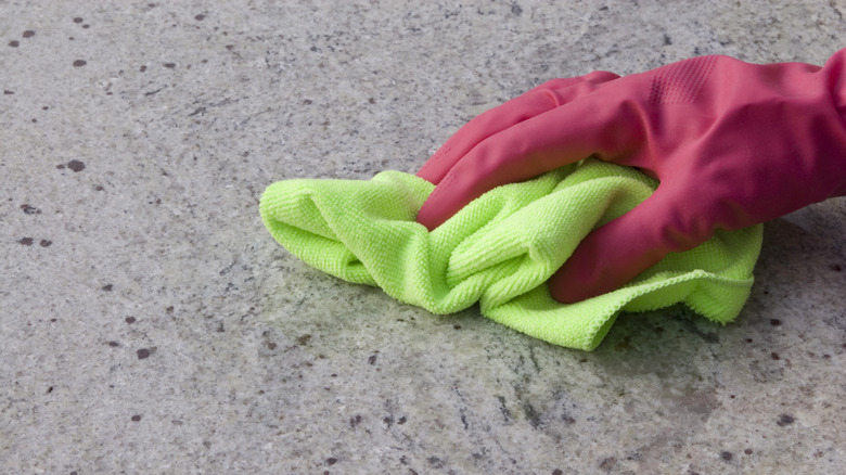 Pink-gloved hand using a light green rag to wipe a granite countertop