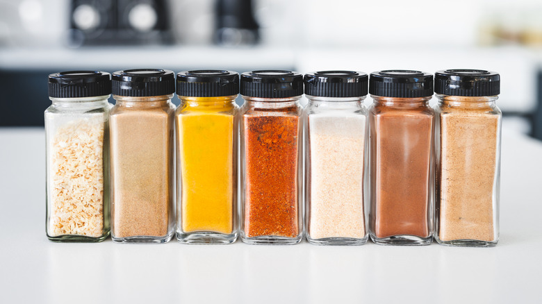 A line up of different seasonings in glass shakers with black lids