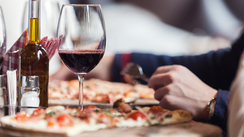 A person eating a pizza and drinking a glass of red wine