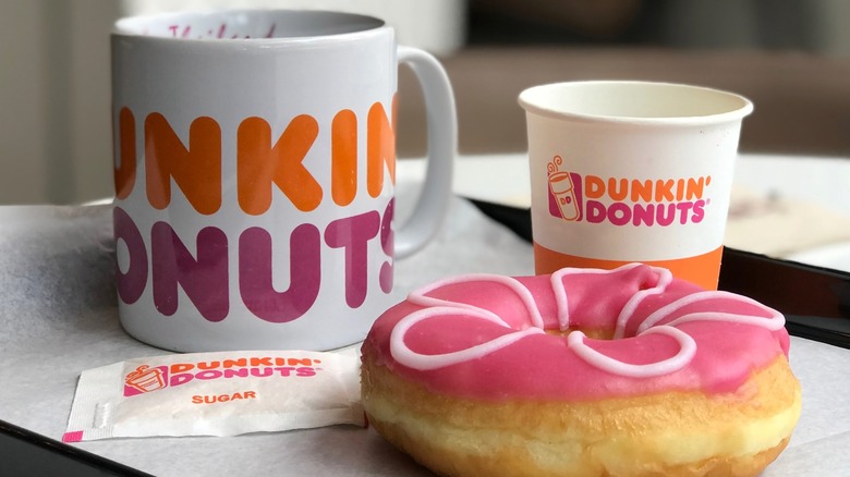 A Dunkin' branded mug and paper cup of coffee next to a donut