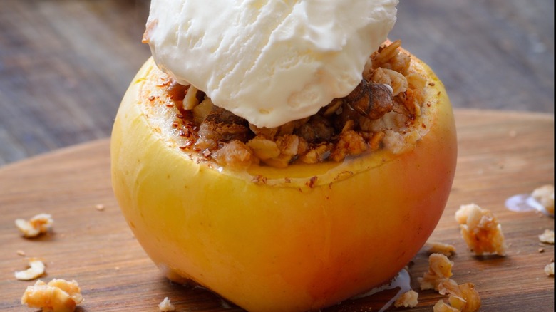 Close up of baked apple with ice cream with walnuts on a cutting board.