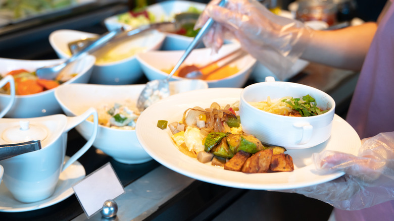 A woman holding plastic gloves scoops food onto her plate at a buffet