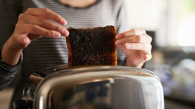 Hands grabbing burnt toast from toaster