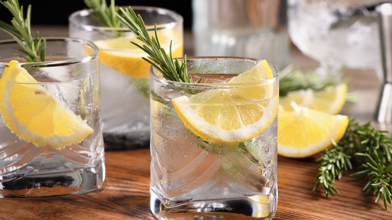 Several glasses of gin and tonics with lemon on a wooden surface