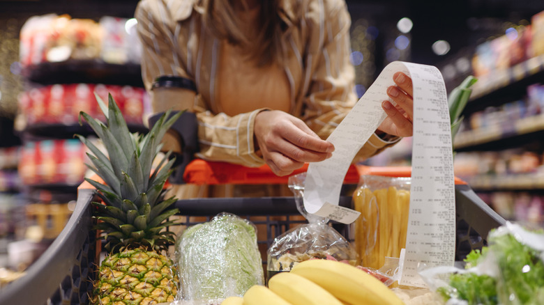 woman at a grocery store checking the receipt with a cart full of groceries