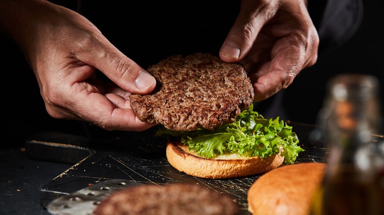 both hands placing burger on lettuce on bun