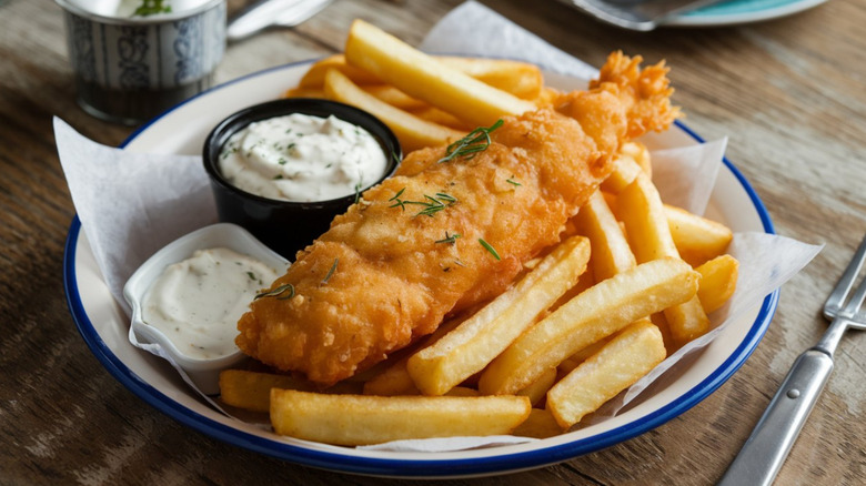 A blue and white plate of fish and chips with tartar sauce on the side.