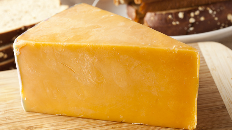 Orange cheddar cheese wedge on wooden cutting board